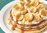 Denny's Salted Caramel Banana Pancakes - two pancakes topped with sliced bananas, vanilla cream, and caramel drizzle.