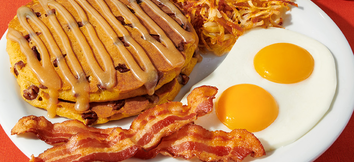 Stack of Denny's Pumpkin pecan pancakes, two strips of bacon, 2 sunny side up eggs and a serving of hashbrowns on a plate. 