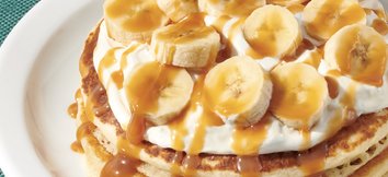 Denny's Salted Caramel Banana Pancakes - two pancakes topped with sliced bananas, vanilla cream, and caramel drizzle.